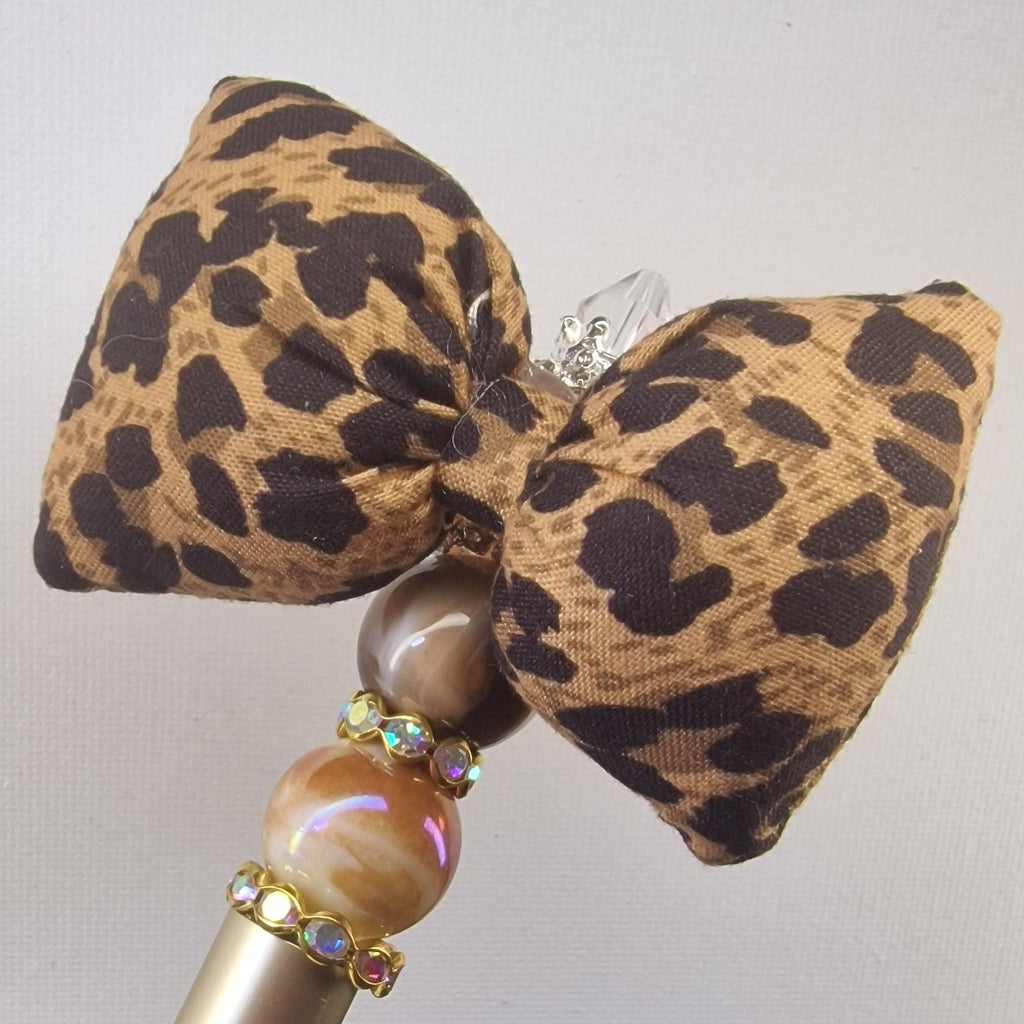 Handversierde goudkleurige pen met zachte strik in panter motief en strass kralen – detailfoto
