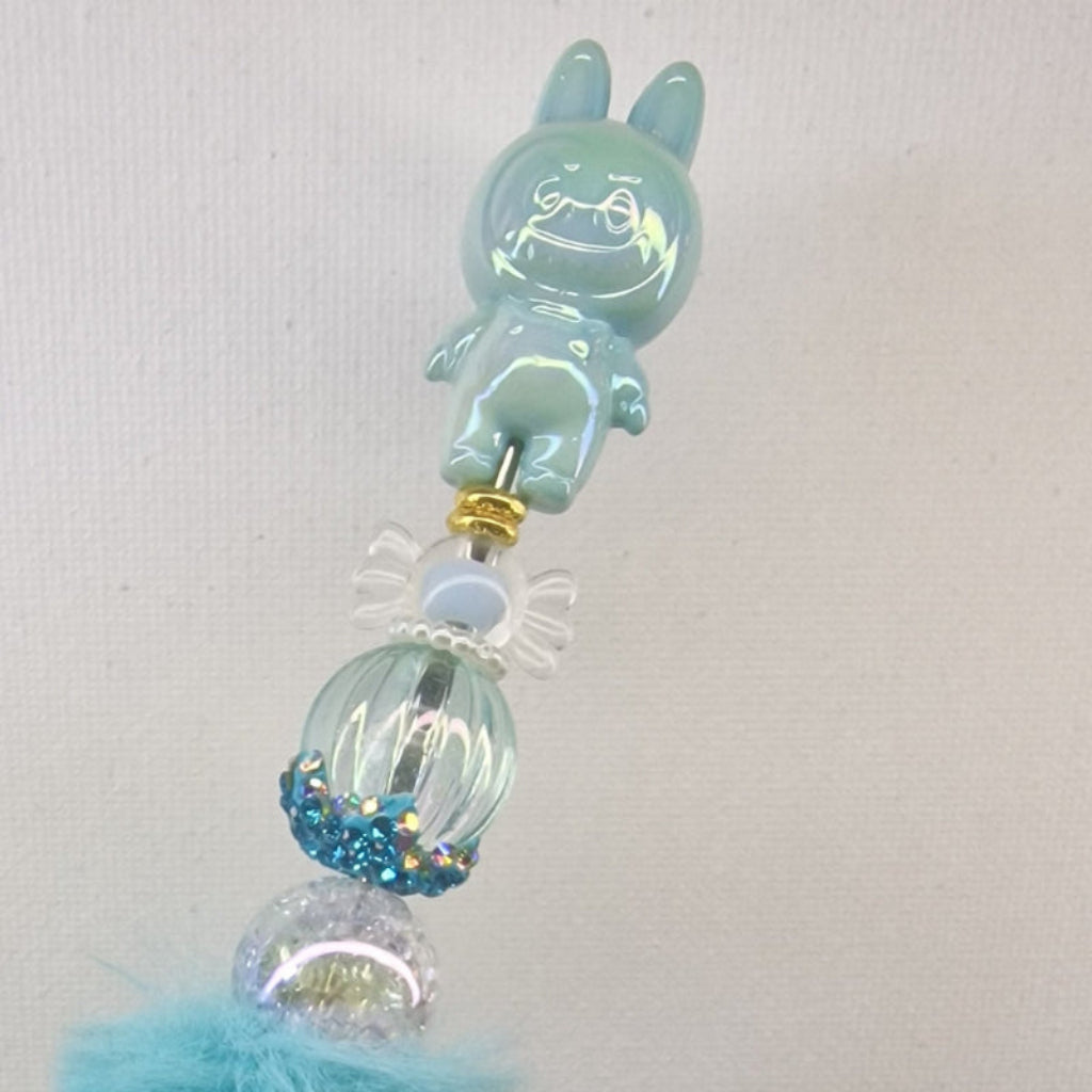 Handversierde turquoise fluffy pen met ondeugend poppetje en blauwe strass kralen – detailfoto
