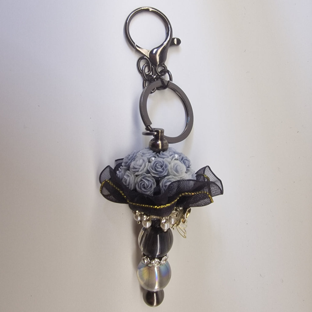 Handversierde zwarte sleutelhanger met lichtblauwe rozen en zilverkleurig vlindertje
