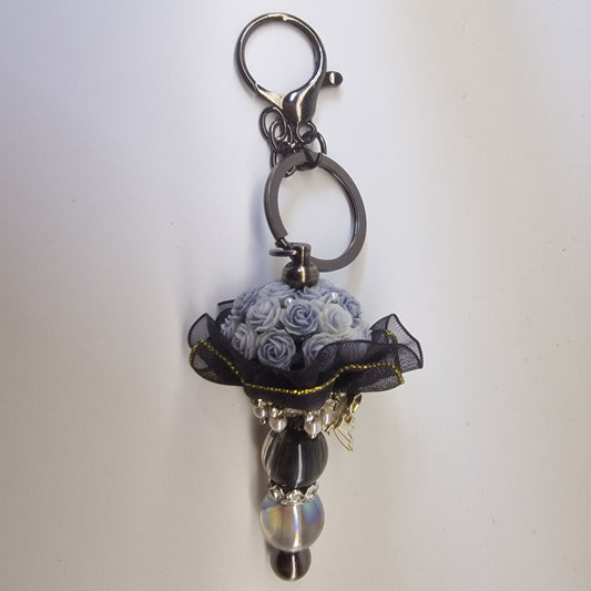 Handversierde zwarte sleutelhanger met lichtblauwe rozen en zilverkleurig vlindertje
